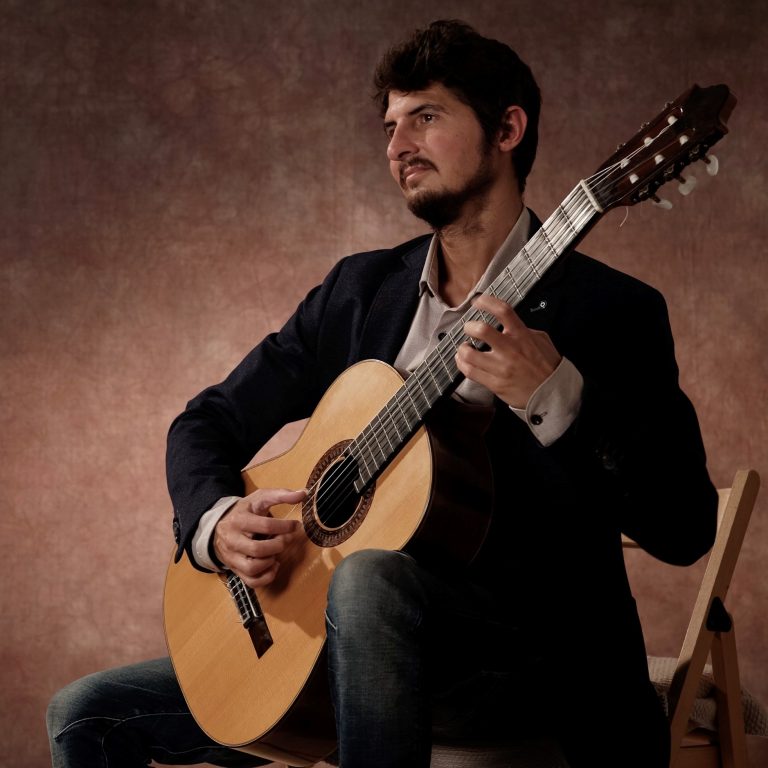 Gitaar docent Silvan de Smit geposeerd met gitaar op stoel
