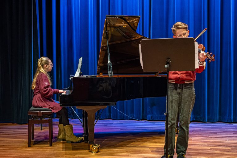 jongedame op piano en jongeman op viool spelen muziekstuk bij revival concert