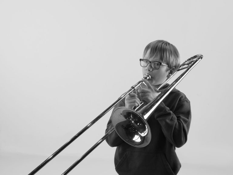 Jongeman poseert met trombone instrument in zwart-wit